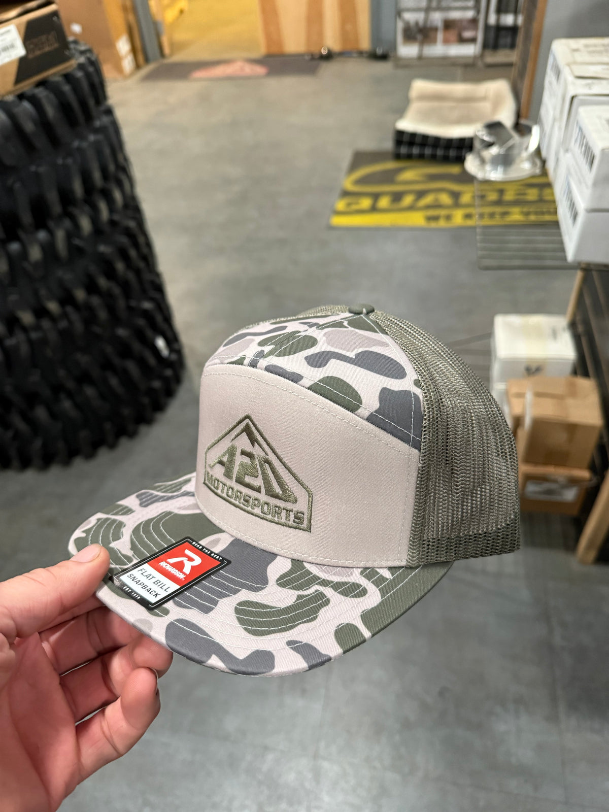 A2D Motorsports trucker hat in duck camo with olive mesh back and tonal embroidered mountain logo