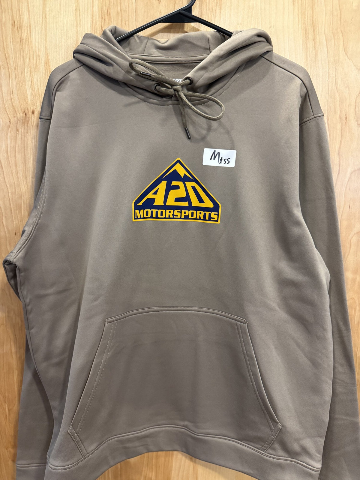 A2D Motorsports sand hoodie with blue and gold mountain logo, hanging