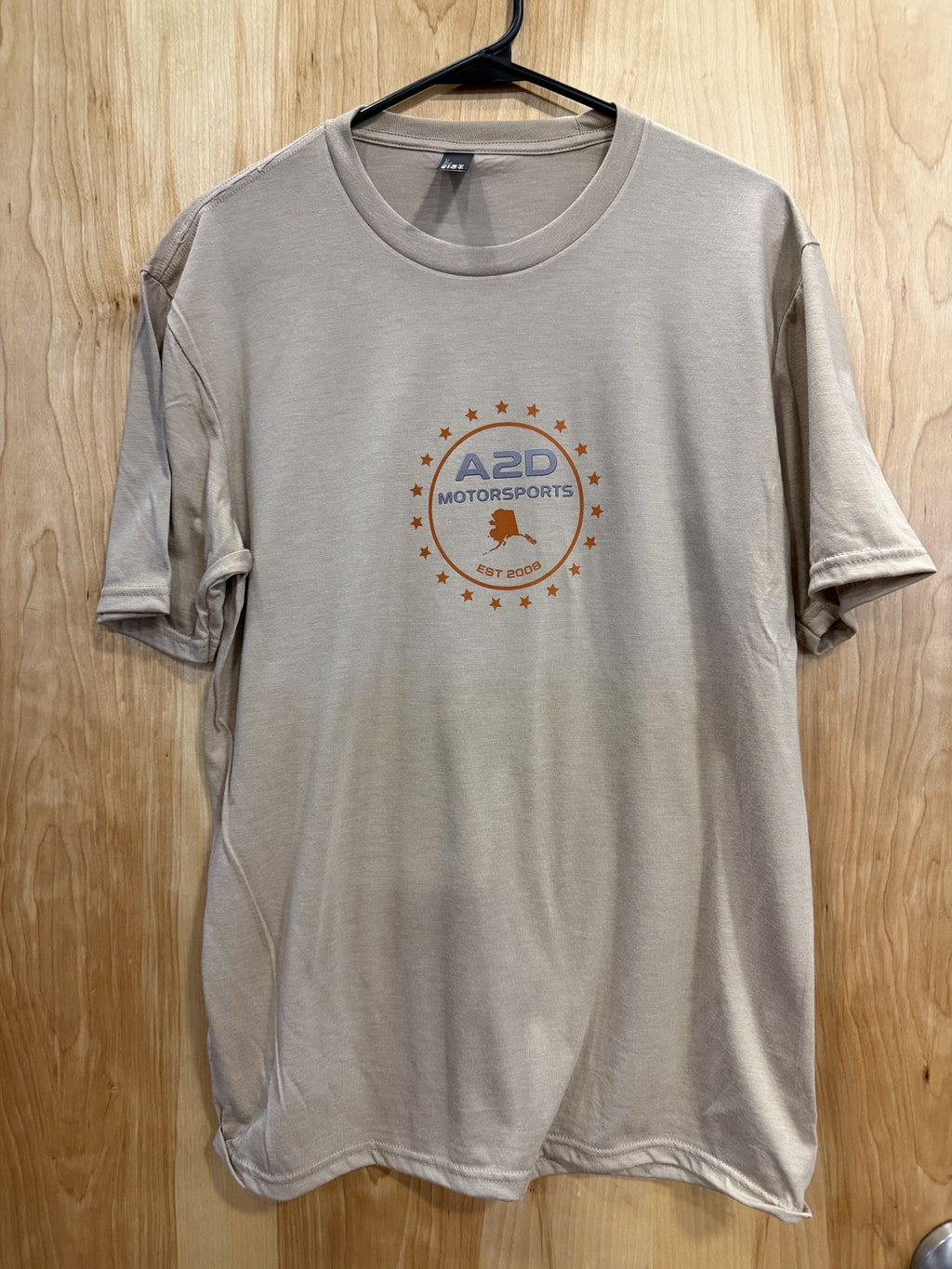 A2D Motorsports sand t-shirt with orange and grey Stars and State Alaska logo, hanging